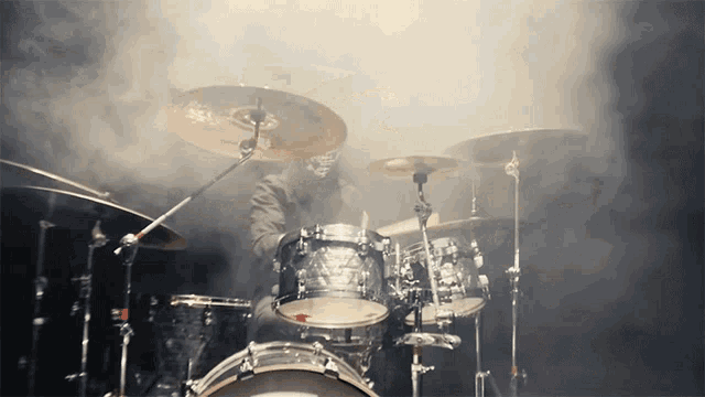 a man in a mask plays drums in a dark room