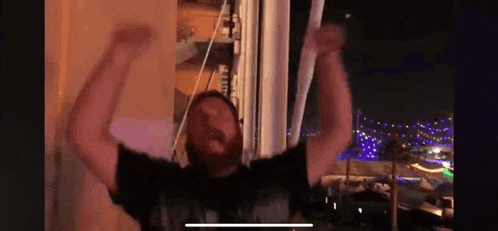 a man with a beard is standing in front of a window with his hands in the air .