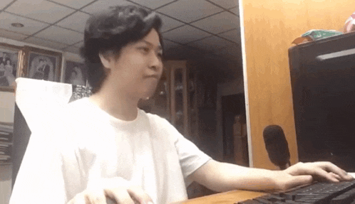 a man in a white shirt is typing on a keyboard in front of a computer monitor