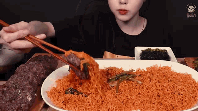 a woman is eating a plate of noodles with chopsticks .