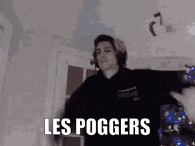a man in a black hoodie is dancing in a room with the words `` les poggers '' written on it .