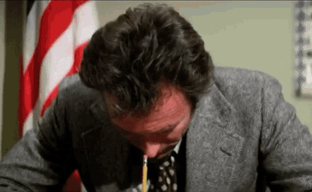 a man in a suit and tie is holding a pencil in his mouth while sitting at a desk .