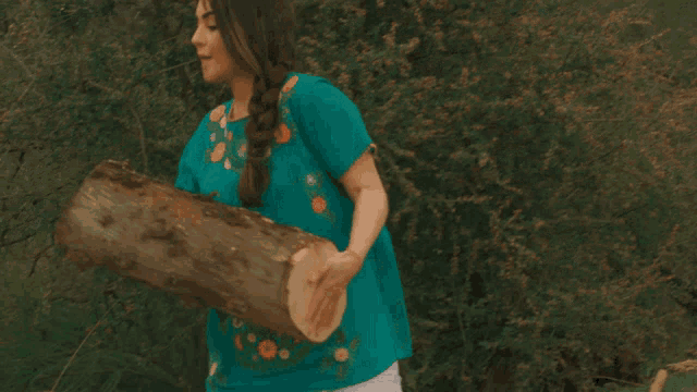 a woman in a teal shirt holds a log in her hands