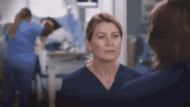a woman in a blue scrub is looking at herself in a mirror in a hospital room .