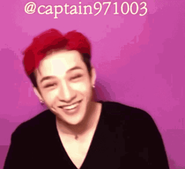 a young man with red hair is smiling in front of a pink background .