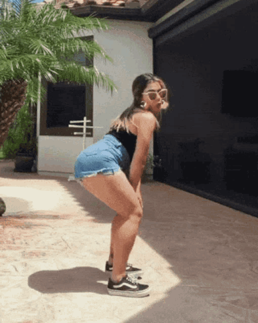 a woman wearing sunglasses and denim shorts is squatting on a patio