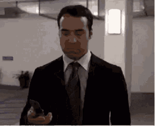 a man in a suit and tie is walking down a hallway while holding a cell phone .