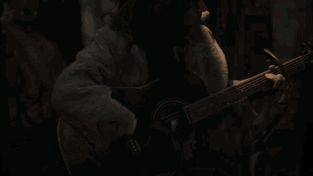 a woman with dark hair and a blue coat is singing into a microphone in a dark room
