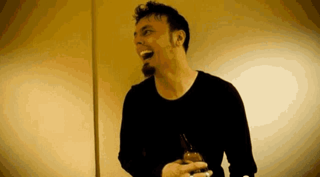 a man in a black shirt is laughing while holding a bottle .