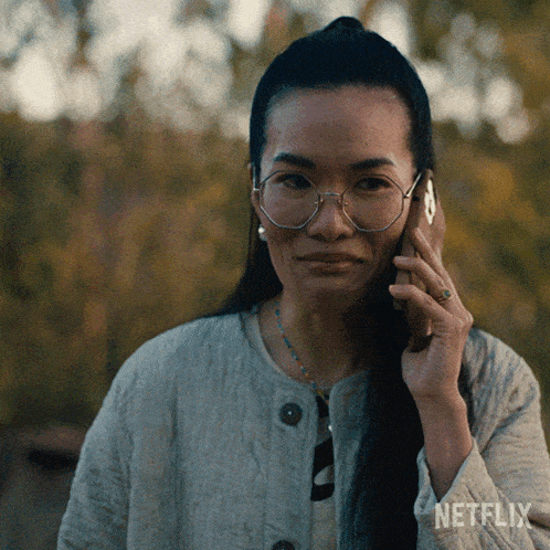a woman wearing glasses is talking on a cell phone with netflix written on the sleeve of her jacket