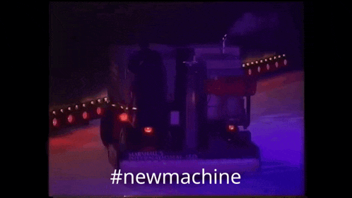 a truck is driving down a snowy road in the dark with the words `` new machine '' written on the bottom .