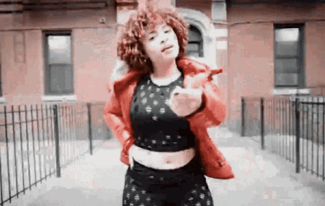 a woman in a red jacket is dancing in front of a building .