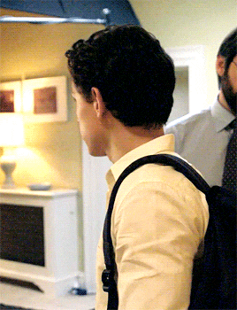 a man wearing a white shirt and a black backpack stands in a room