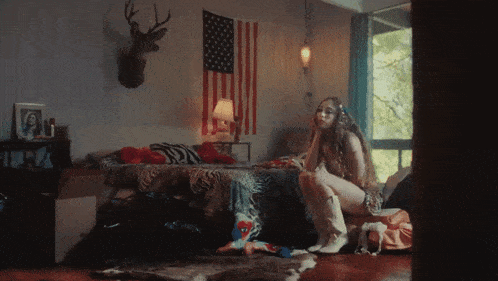 a woman sits on a bed with an american flag hanging on the wall behind her