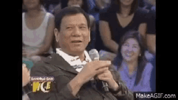 a man in a suit is sitting in front of a microphone and making a funny face .