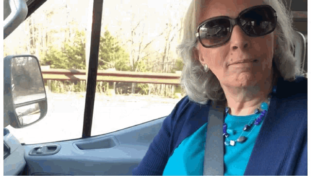 a woman wearing sunglasses and a blue shirt is sitting in the driver 's seat of a car
