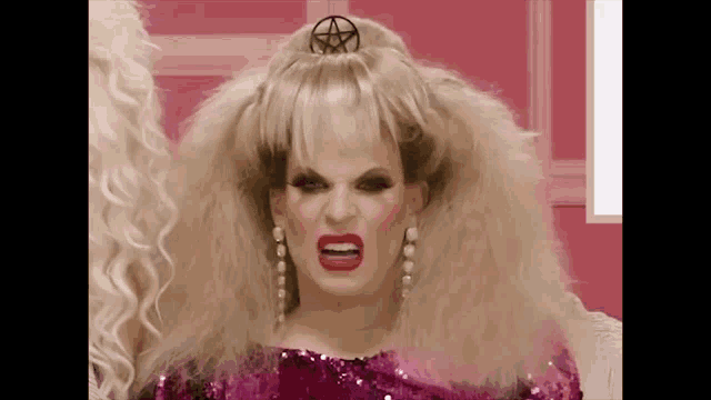 a drag queen with a pentagram in her hair is wearing a pink dress and earrings .