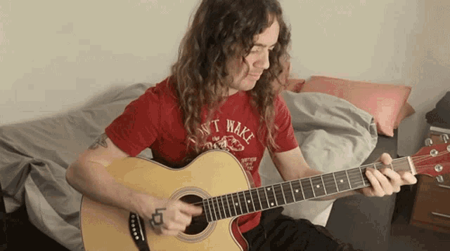 a man with long hair is playing an acoustic guitar while wearing a red shirt that says ' dont wake ' on it