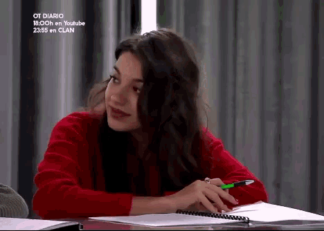 a woman in a red sweater is sitting at a desk with a notebook and a pen in her hand