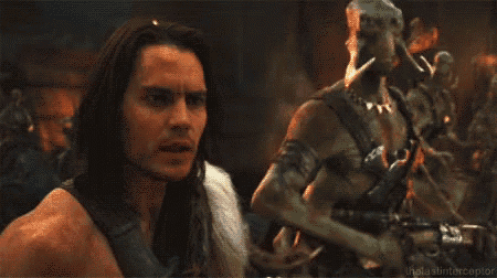 a man with long hair is standing next to a statue of a man with horns .