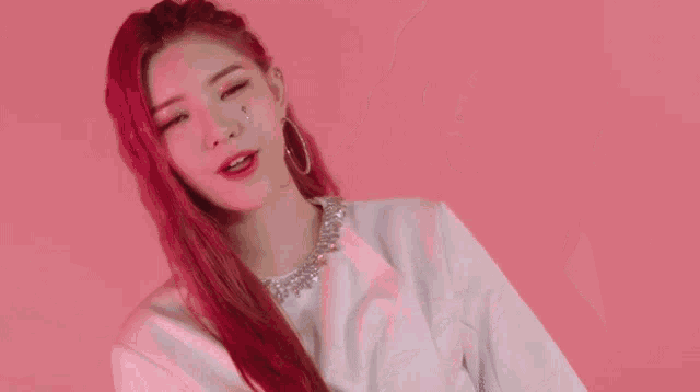 a woman with red hair and hoop earrings is wearing a white top and earrings .