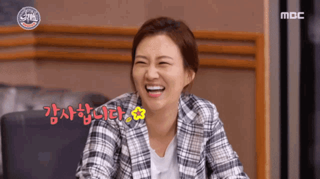 a woman in a plaid jacket is laughing in front of a mbc sign