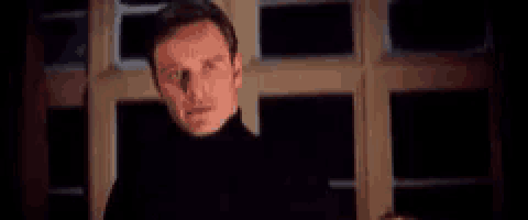 a man in a black turtleneck is standing in front of a window with the word perfection written above him .