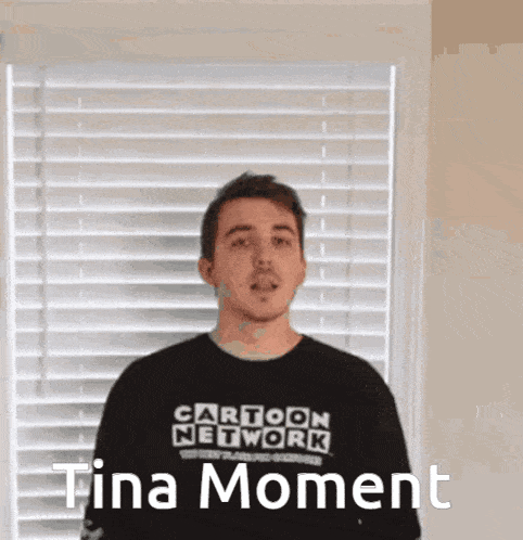 a man wearing a cartoon network t-shirt stands in front of a window