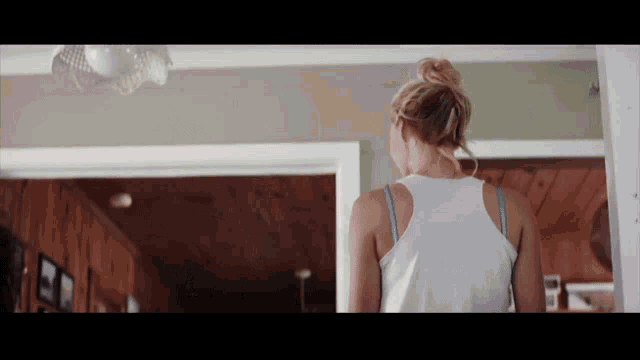 a woman in a white tank top is standing in a room