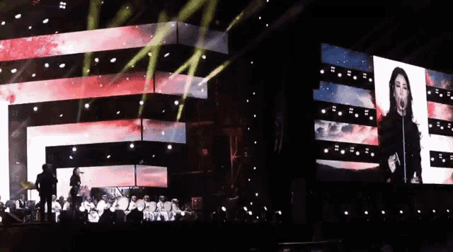 a woman singing in front of a large screen that says ' e '