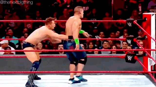 two men are wrestling in a wrestling ring while a crowd watches .