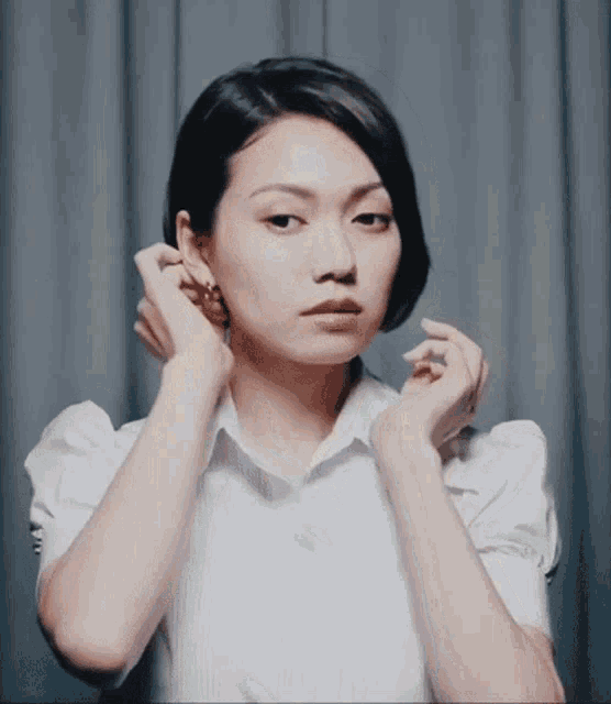 a woman in a white shirt adjusts her earring