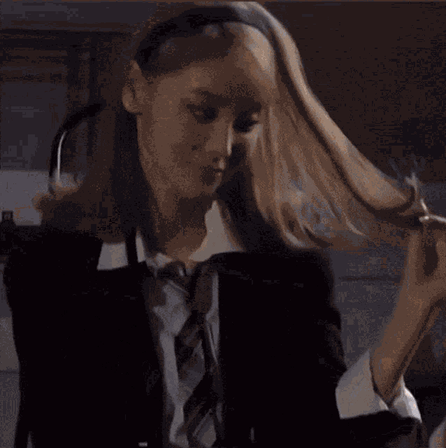 a woman wearing a suit and tie is holding her hair .