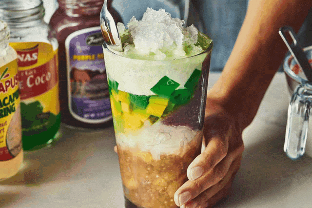 a person is holding a glass of ice cream with a jar of purple jam in the background