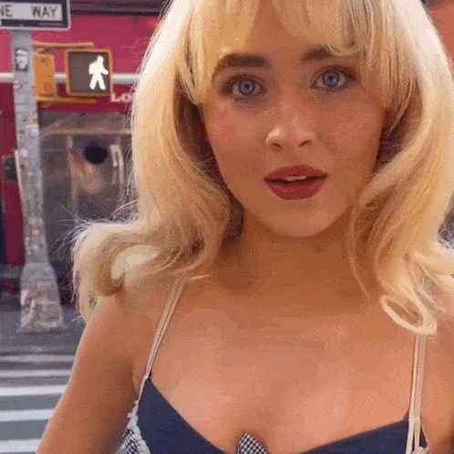 a woman with blonde hair is standing in front of a crosswalk sign that says one way