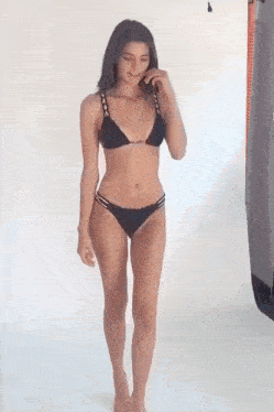 a woman in a black bikini is walking on a white surface