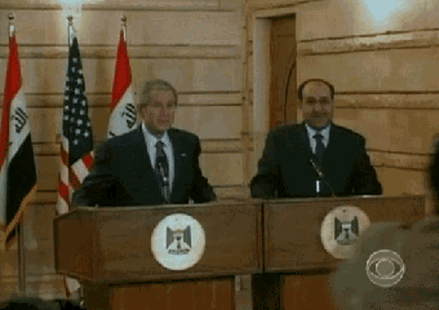 a man in a suit and tie stands at a podium with a logo that says iraq