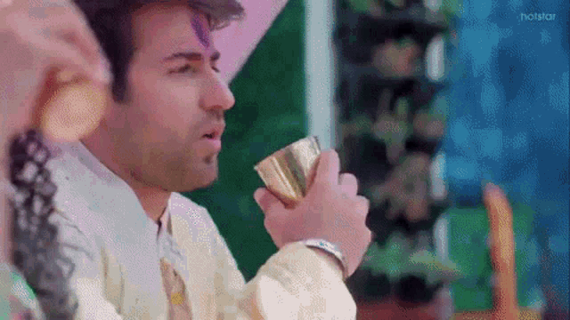 a man is drinking from a gold cup while wearing a pink hat .