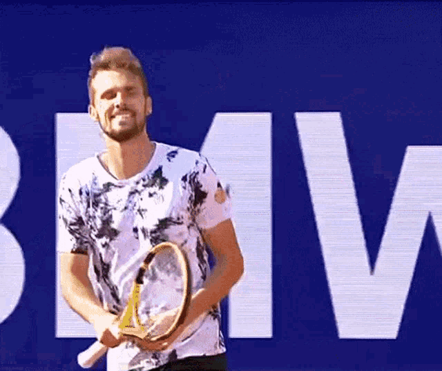 a man is holding a tennis racquet in front of a sign that says bmv