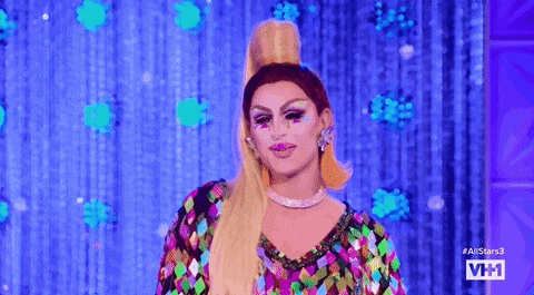 a drag queen is standing on a stage wearing a colorful sequined dress .