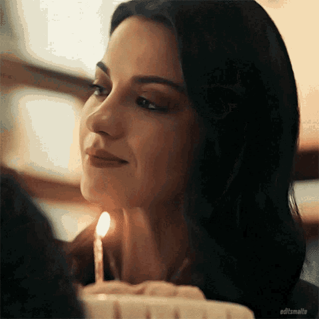a woman is smiling while holding a candle in front of her face .