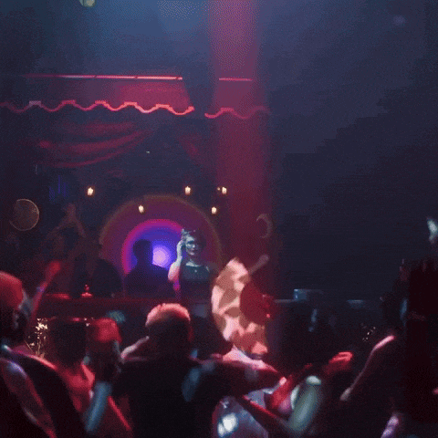 a group of people are dancing in a dark room with a dj in the background