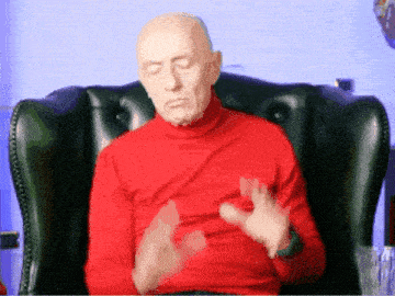 a bald man wearing a red turtleneck is sitting in a chair with his eyes closed