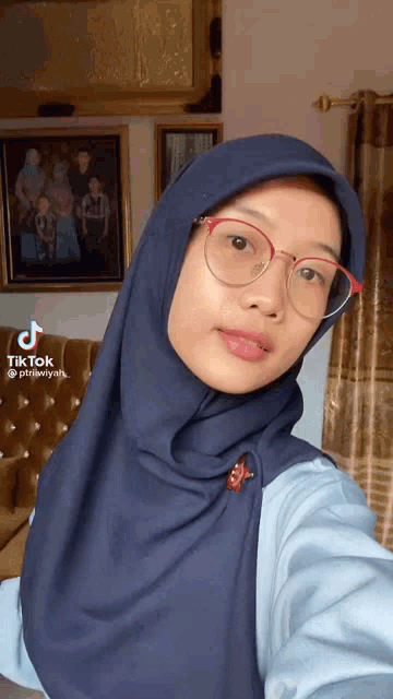a woman wearing glasses and a blue hijab takes a selfie