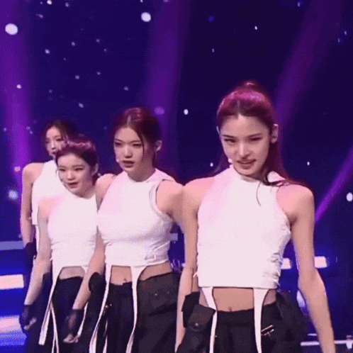 a group of young women are standing on a stage wearing white tank tops and black pants