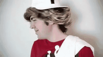 a young man wearing a red shirt and a white hat is standing in front of a white wall .