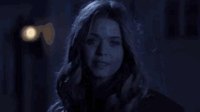 a woman in a dark room with her hair blowing in the wind looks at the camera