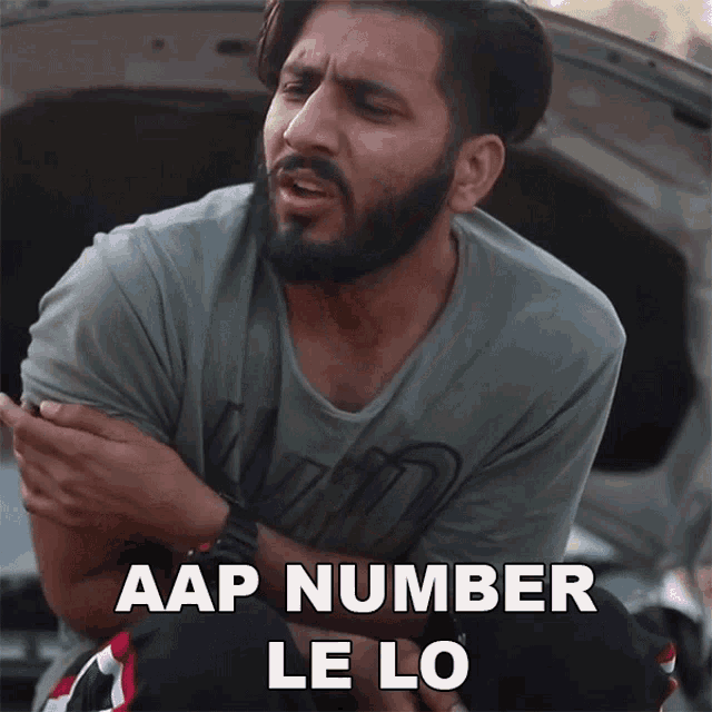 a man with a beard is sitting in the back of a car with the hood open and says aap number le lo