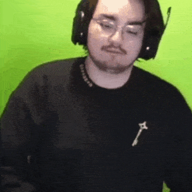 a man wearing headphones and a black shirt is sitting in front of a green background .