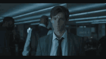 a young man in a suit and tie is standing in a dark room looking at the camera .
